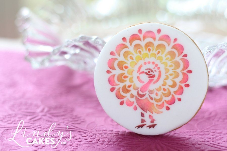 pink-peacock-stencilled-onto-sugarpaste-on-a-round-biscuit-by-cake-designer-lindy-smith