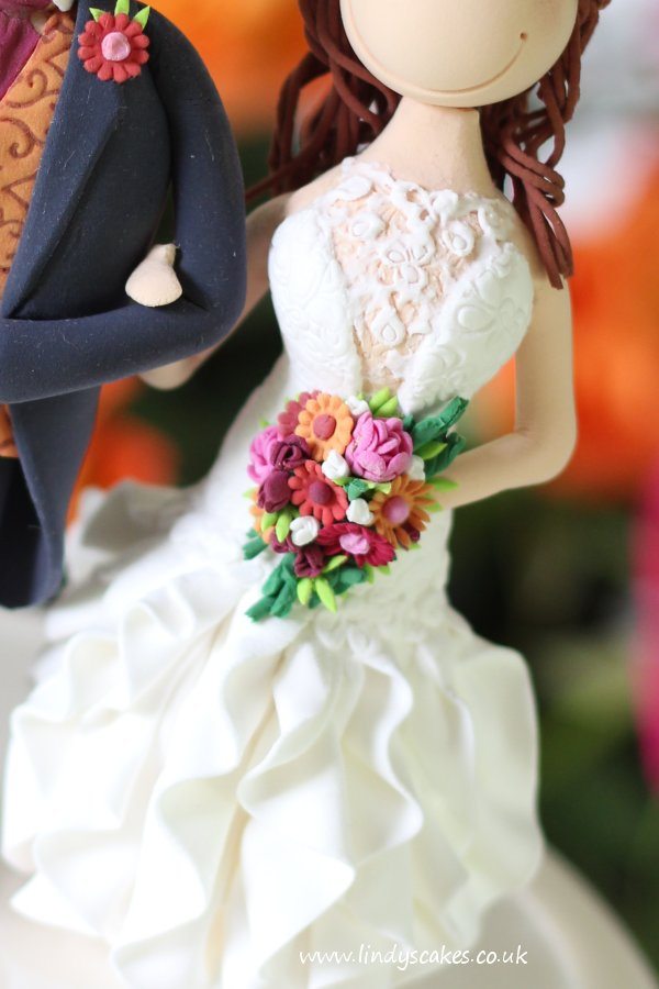 Miniature hand modelling flowers make up the bouquet on this bride and groom cake topper by Lindy Smith