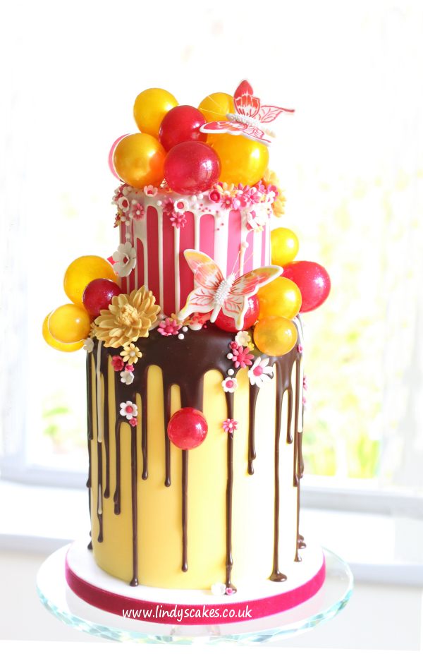 Fuchsia pink and metallic edible gelatin baubles adorn this striking chocolate drip cake